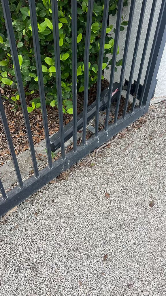 Black metal gate with motor, green bushes, and gravel driveway. in Los Feliz, CA