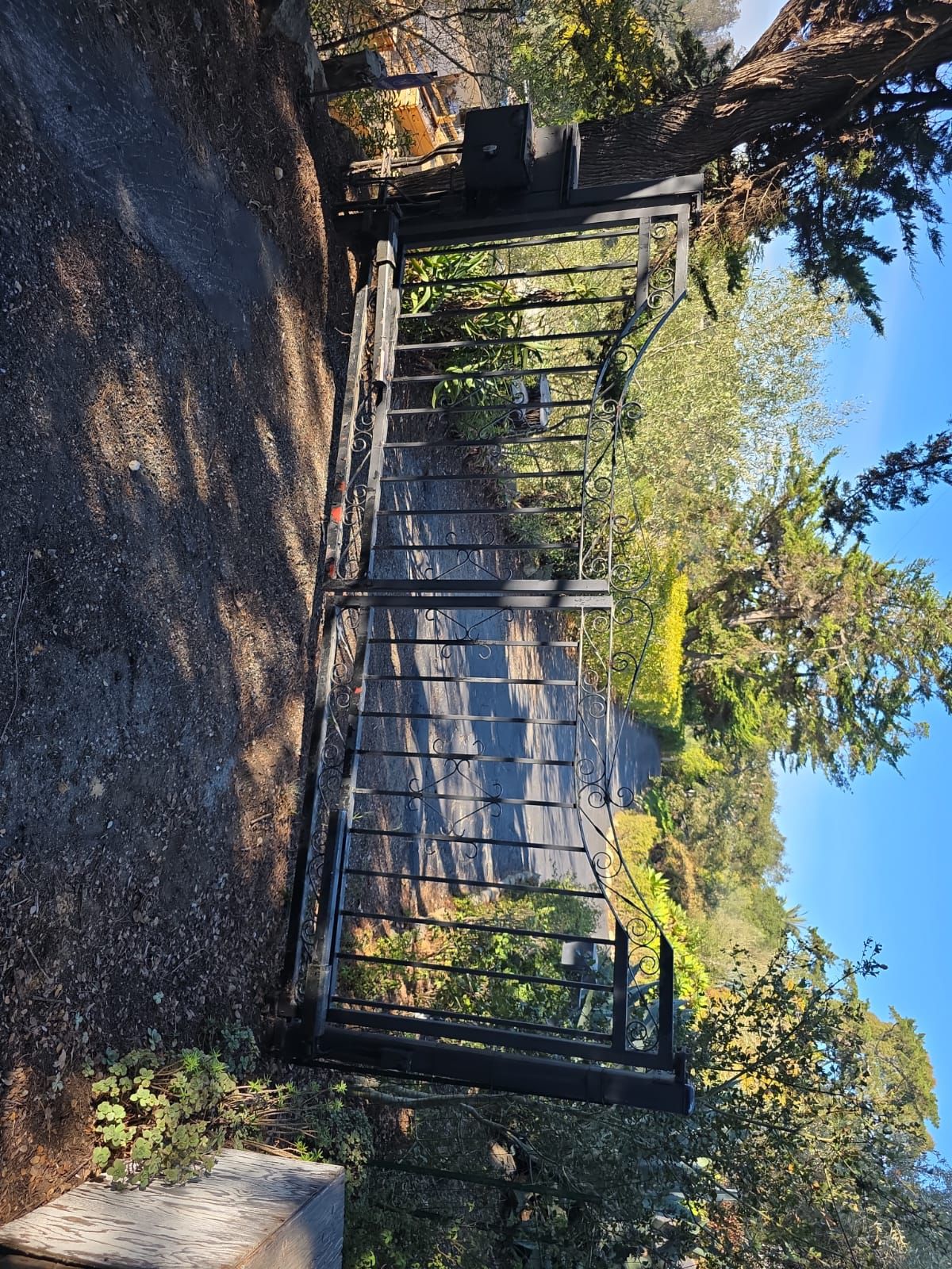 Black metal gate with automatic opener, driveway entrance, trees, blue sky. in Los Feliz, CA
