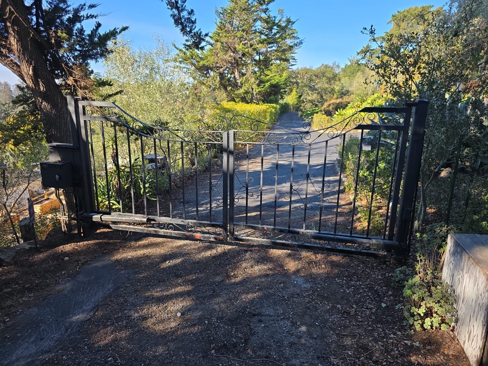 Black ornamental metal gate open to paved driveway with trees in West Hollywood, CA